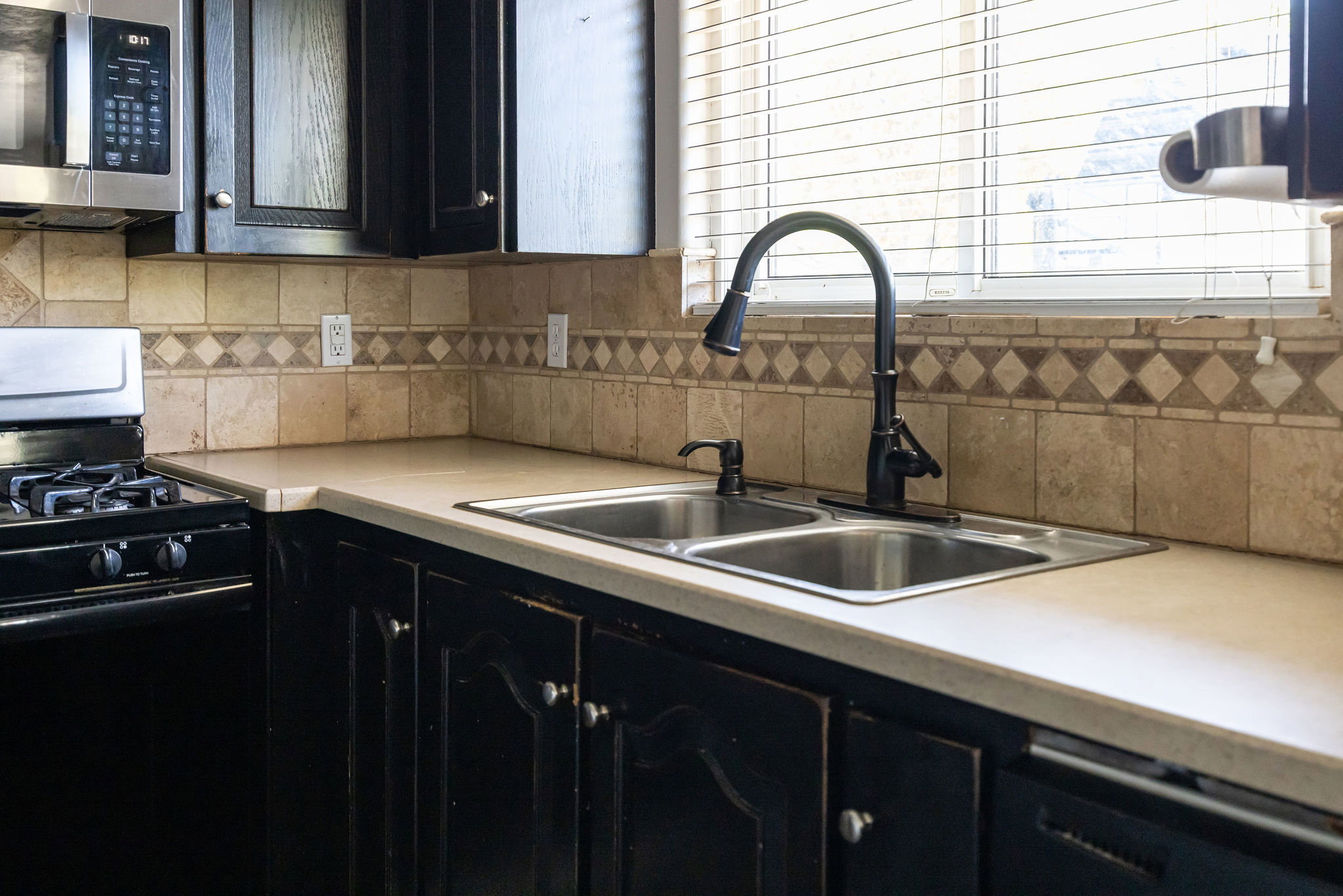 Kitchen with dark cabinetry, black gas stove, stainless steel microwave, light countertops, and decorative backsplash
