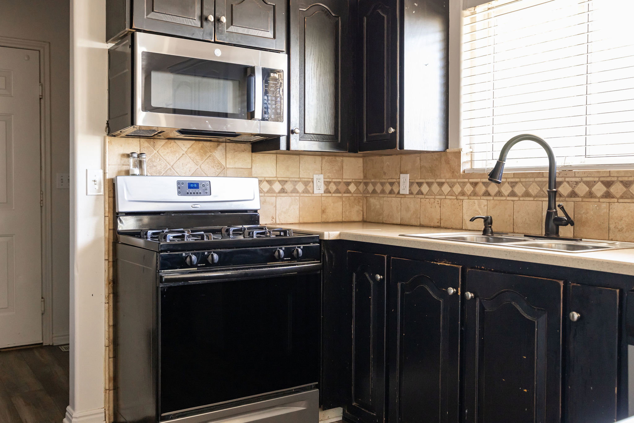 Kitchen with gas stove, light countertops, stainless steel microwave, and decorative backsplash