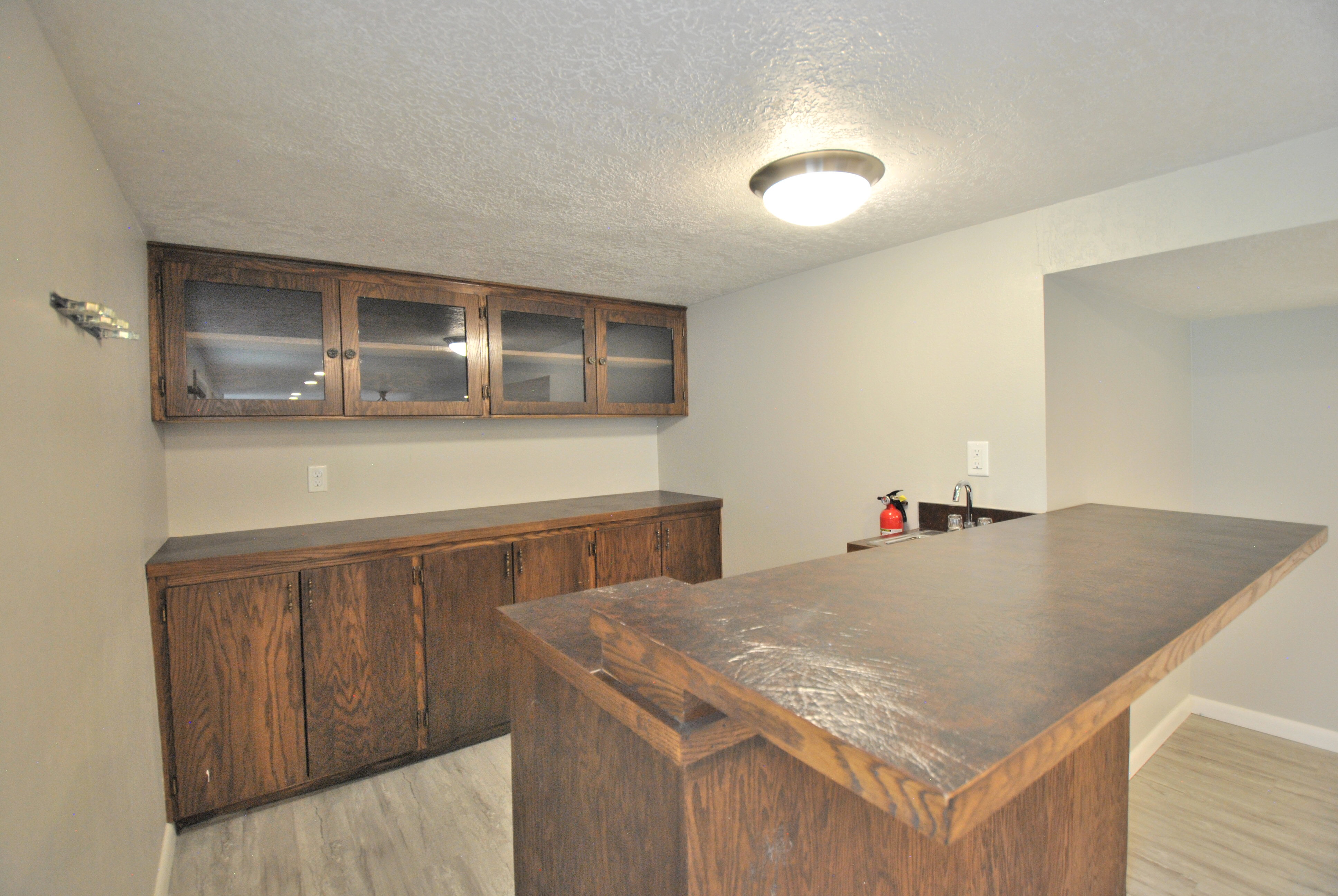 Indoor dry bar featuring light wood-type flooring, a textured ceiling, glass insert cabinets, and wood finish cabinets