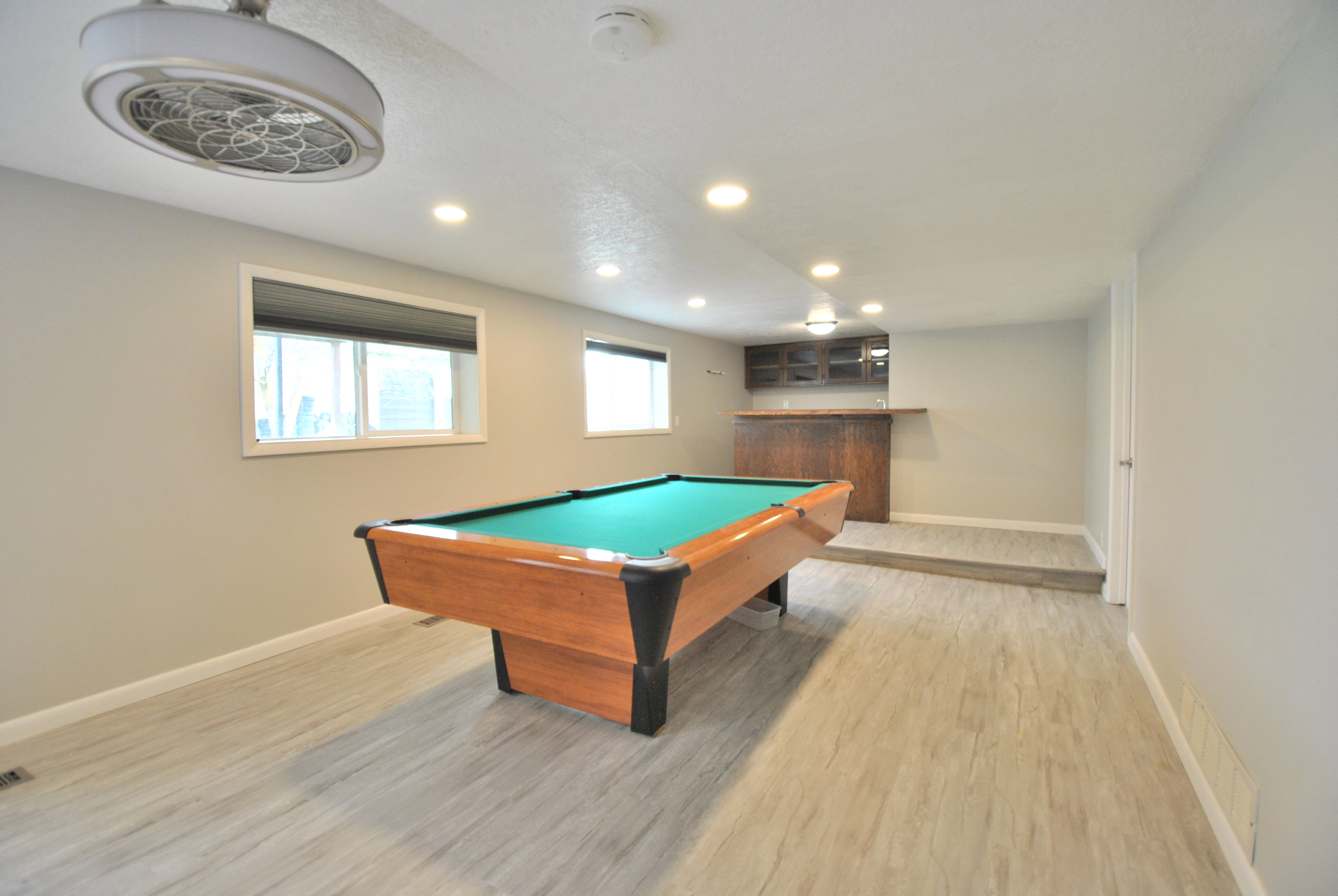 Family room with light wood-style flooring, recessed lighting, pool table (included), and wet bar beyond.