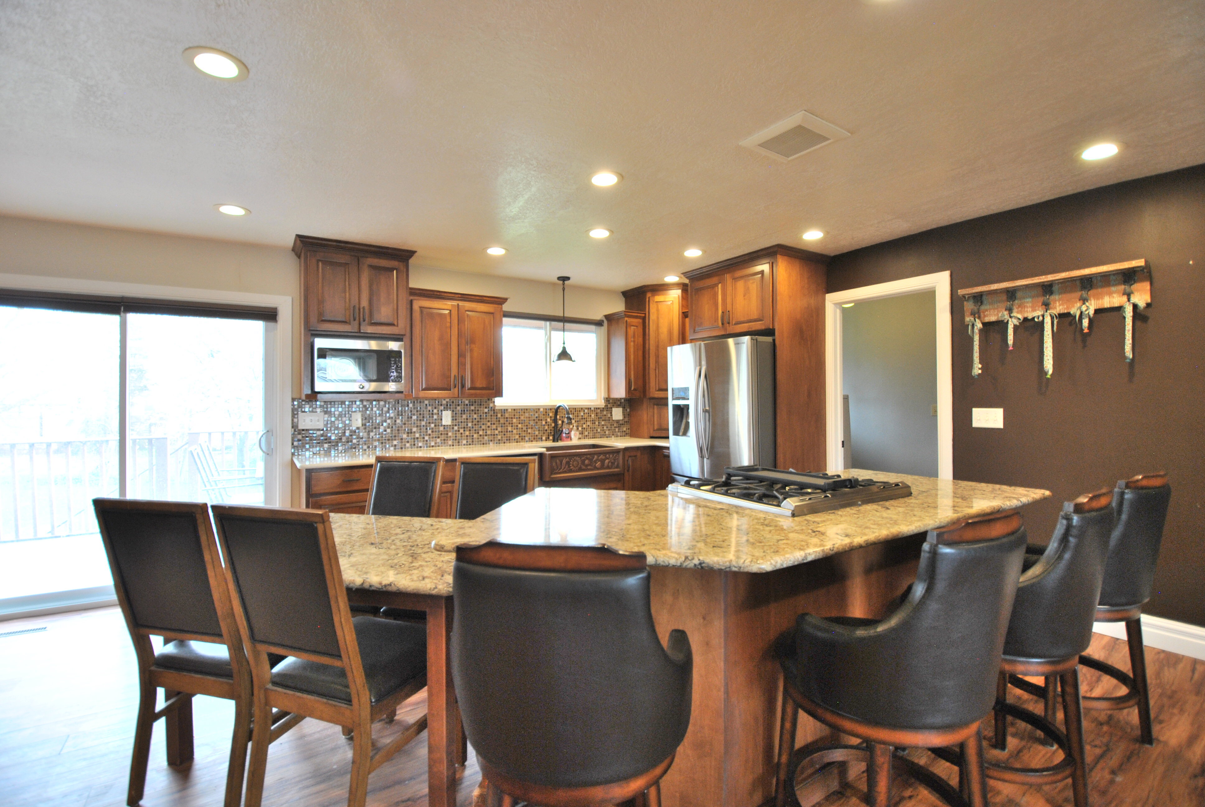 Kitchen featuring dark wood-style flooring, decorative backsplash, light stone counters, and stainless steel appliances.  The side table can be a dining room table or an extension to the countertop