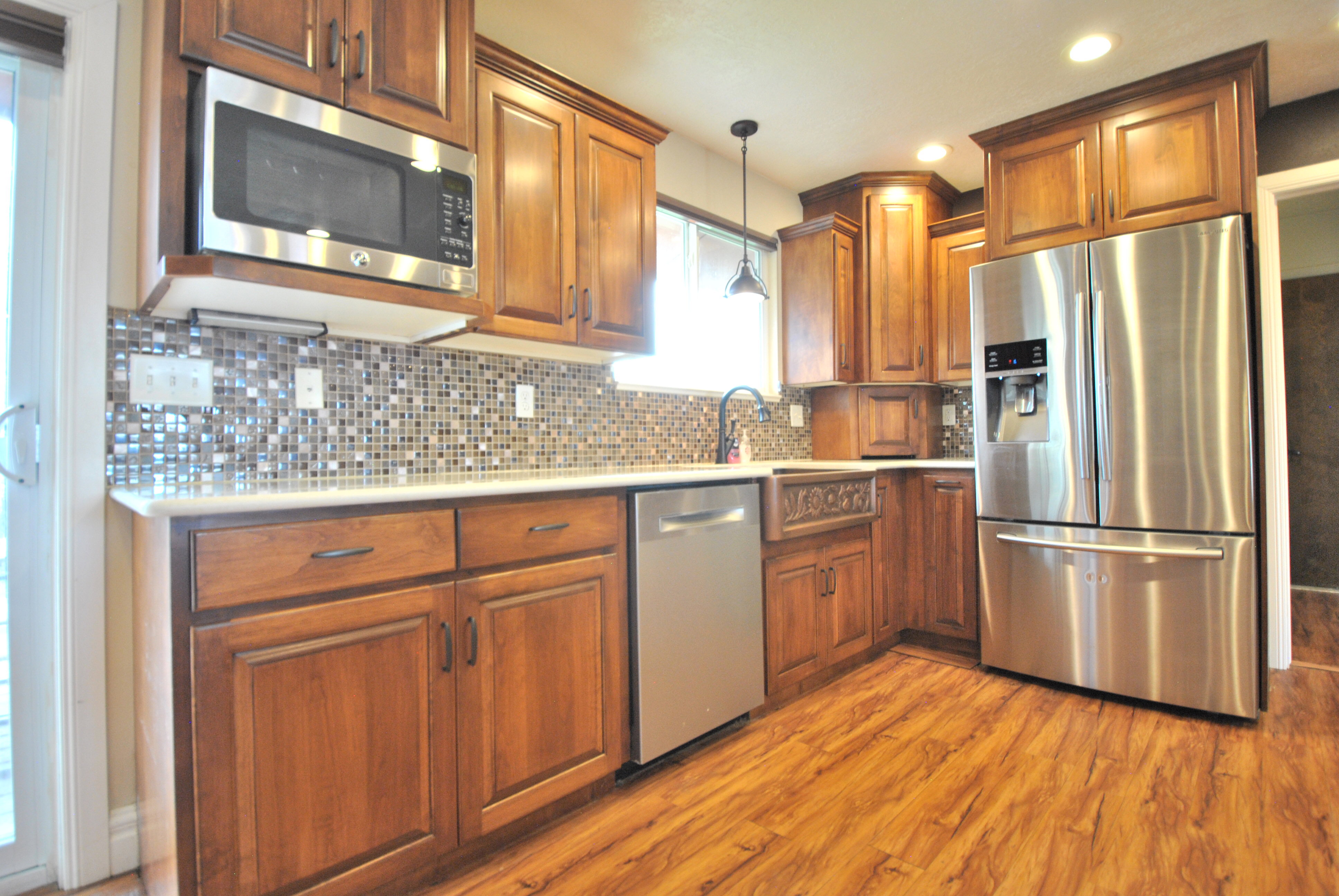 Kitchen featuring stainless steel appliances, wood finish cabinetry, hanging light fixtures, light wood finished floors, and decorative backsplash