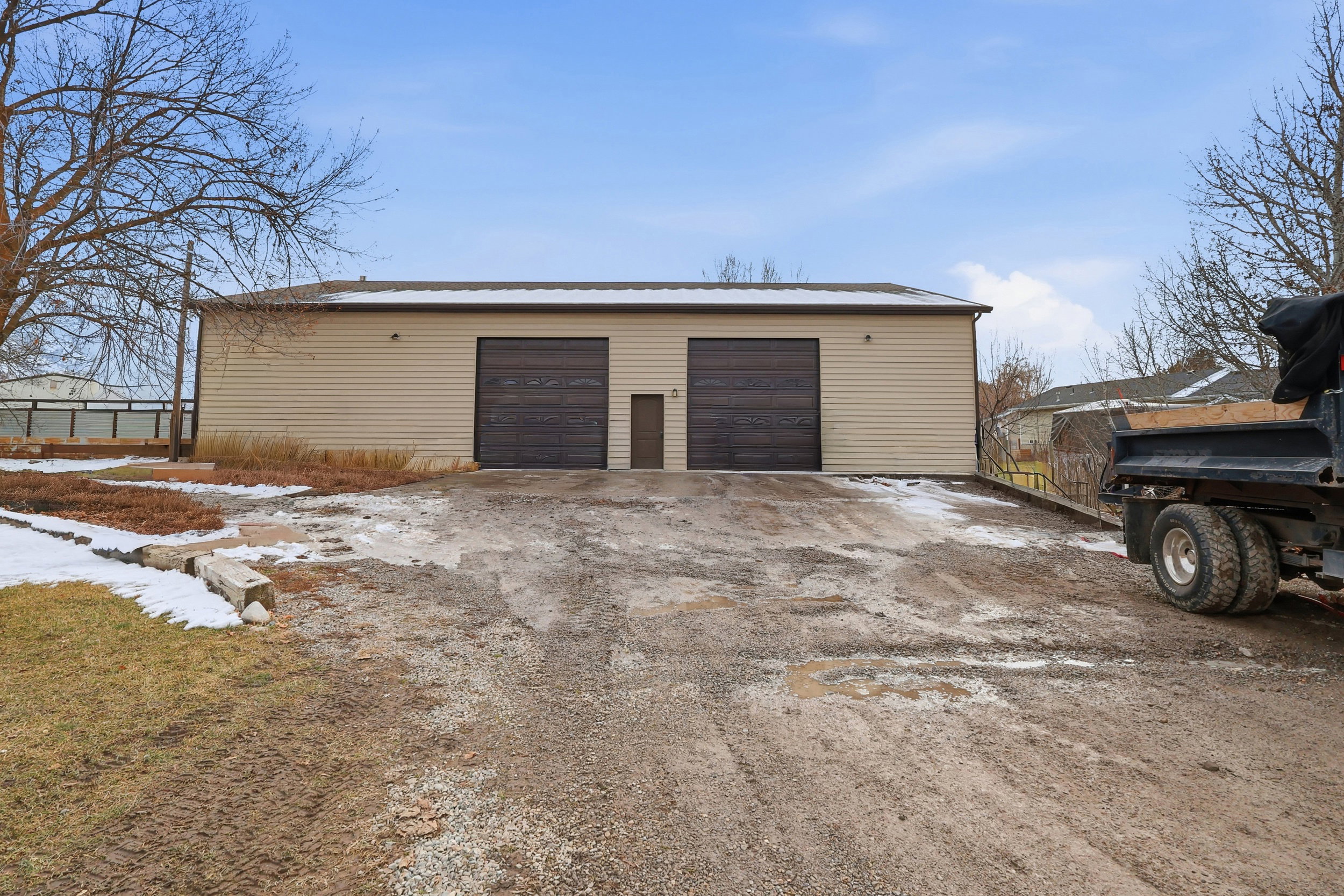 Detached beige siding structure featuring two roll-up doors and a separate entry door