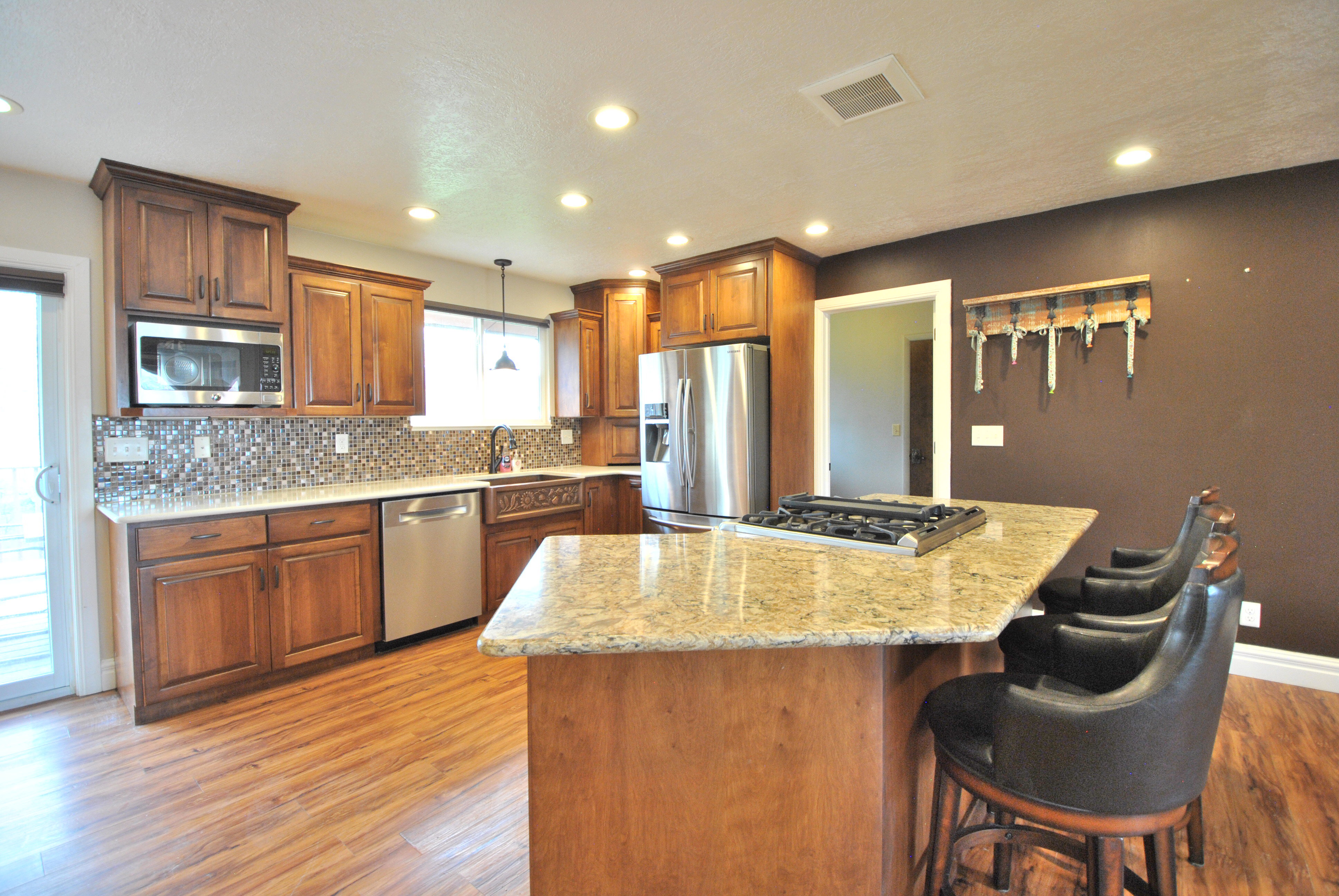 Kitchen featuring stainless steel appliances, light stone countertops, backsplash, light wood-type flooring, and wood finish cabinetry