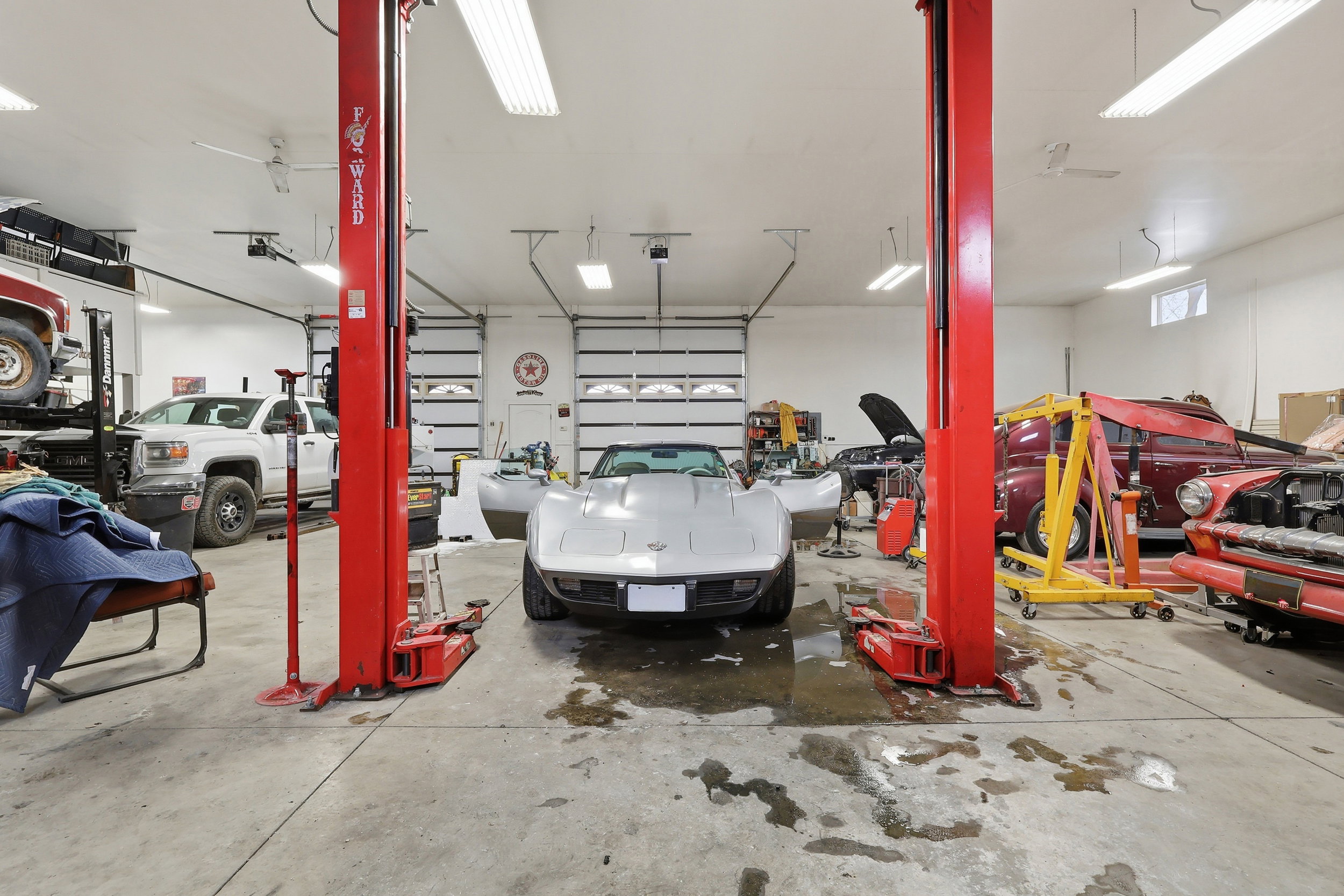 Spacious garage featuring a concrete floor, two vehicle lifts, multiple overhead garage doors, bright ceiling-mounted strip lighting, and transom windows