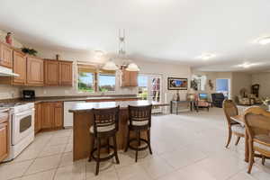 Kitchen with a kitchen island, white appliances, a kitchen bar, light tile patterned floors, and dark countertops