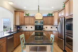 Kitchen featuring dark stone counters, stainless steel appliances, light wood-style floors, and a kitchen island