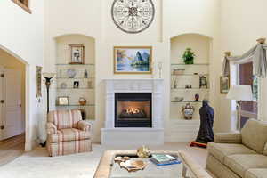 Carpeted living area with built in shelves, a glass covered fireplace, and a high ceiling