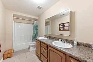 Bathroom featuring double vanity, a textured ceiling, shower / bath combo with shower curtain, and light tile patterned floors