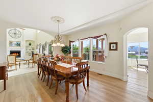 Dining space with arched walkways, light wood-type flooring, a chandelier, a warm lit fireplace, and built in features