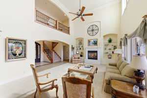 Living room featuring built in shelves, a glass covered fireplace, a ceiling fan, ornamental molding, and light carpet
