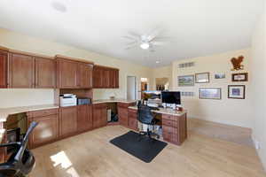 Office space with built in study area, a ceiling fan, and light wood finished floors
