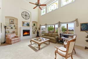 Carpeted living area with healthy amount of natural light, a warm lit fireplace, built in shelves, ceiling fan, and ornamental molding