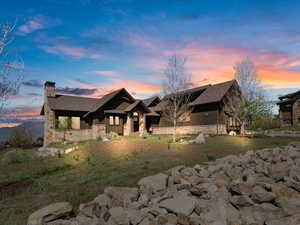 View of front facade with stone siding, a chimney, and a shingled roof