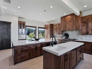 Kitchen featuring glass insert cabinets, backsplash, recessed lighting, light stone counters, and beam ceiling