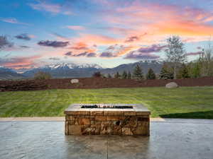 Patio terrace at dusk featuring a fire pit, a mountain view, and a lawn
