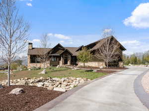 View of front facade with stone siding, a chimney, board and batten siding, a front lawn, and a porch