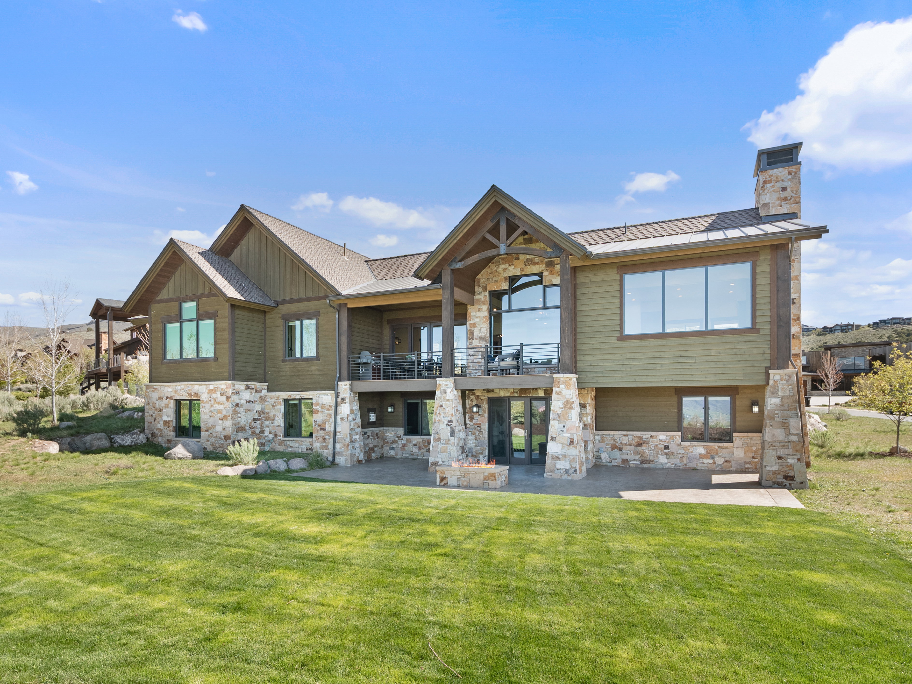 Back of property featuring stone siding, a balcony, and a yard