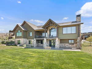 Back of property featuring stone siding, a balcony, and a yard