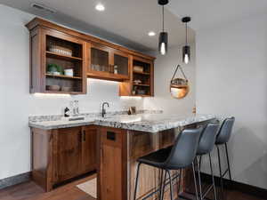 Bar area with open shelves, dark wood finished floors, pendant lighting, light stone countertops, and wood finish cabinetry