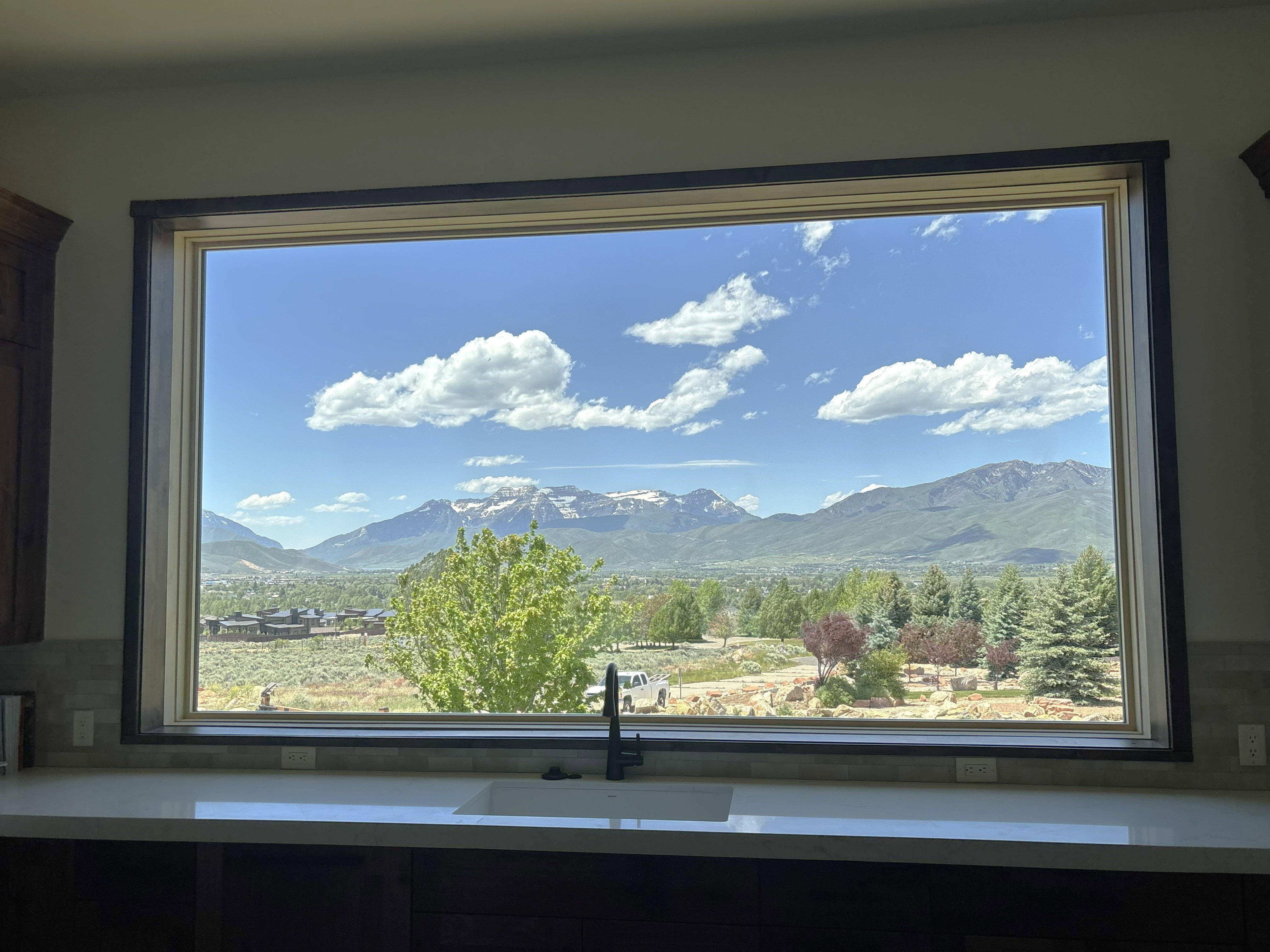 Panoramic window with mountain and valley scenery, featuring a white undermount sink, a matte black gooseneck faucet, light-colored countertops, and a subway tile backsplash