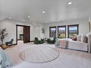 Bedroom with a barn door, light colored carpet, recessed lighting, and ensuite bathroom
