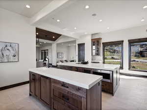 Kitchen featuring glass insert cabinets, lofted ceiling with beams, light stone countertops, recessed lighting, and open floor plan