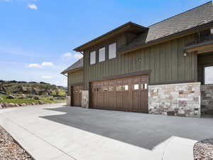 View of home's exterior featuring stone siding, concrete driveway, board and batten siding, and a garage