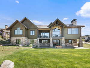 Back of house featuring stone siding, a balcony, and a yard