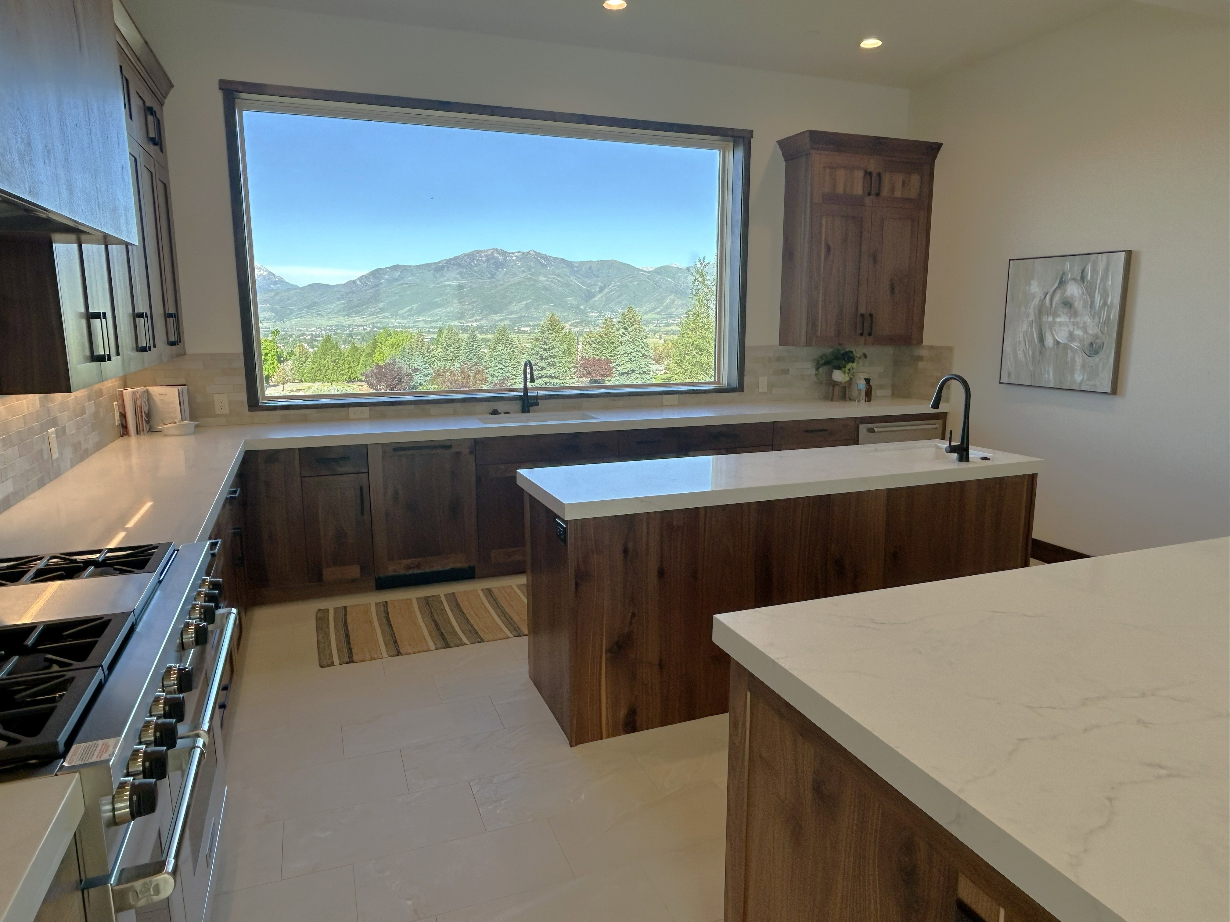 Expansive kitchen featuring a large picture window, two central islands with stone countertops, wood-finish cabinetry, and a professional-grade range