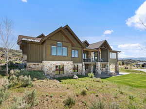 View of front of home featuring stone siding, a balcony, a front lawn, and a mountain view