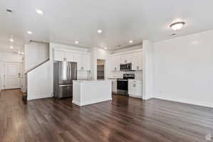Kitchen featuring stainless steel appliances, white cabinets, dark wood-style floors, an island with sink, and recessed lighting