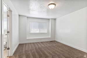 Unfurnished room with a textured ceiling and dark colored carpet