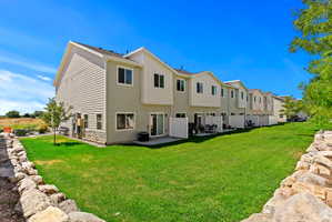 Rear view of house featuring board and batten siding, a lawn, stone siding, and a patio