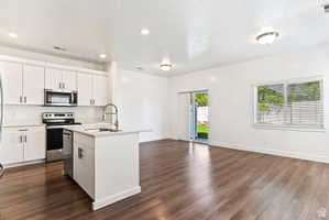 Kitchen featuring an island with sink, stainless steel appliances, white cabinetry, dark wood finished floors, and a textured ceiling