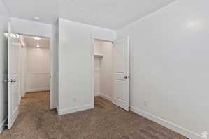 Unfurnished bedroom with dark carpet, a spacious closet, and a textured ceiling
