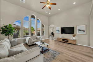 Living area with arched walkways, ceiling fan, a high ceiling, light wood-style flooring, and recessed lighting