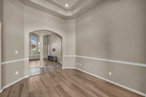 Unfurnished room with arched walkways, wood finished floors, and a tray ceiling