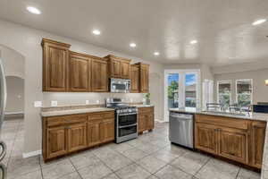 Kitchen featuring arched walkways, wood finish cabinetry, stainless steel appliances, light stone counters, and light tile patterned floors
