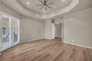 Unfurnished bedroom with a tray ceiling, access to exterior, a ceiling fan, recessed lighting, and light wood-style floors