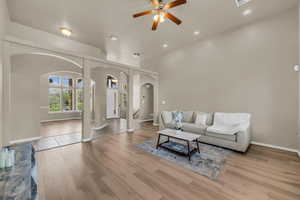Living room with arched walkways, light wood finished floors, ceiling fan, a high ceiling, and recessed lighting
