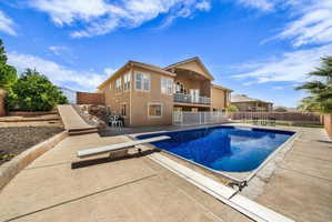 View of pool featuring a balcony, patio surround, a fenced backyard, and a diving board