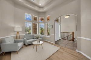Living area featuring arched walkways, light wood-style floors, a tray ceiling, and an upstairs landing