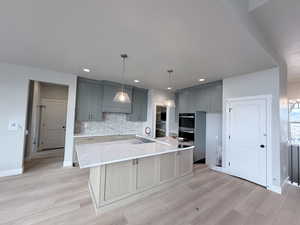 Kitchen featuring gray cabinetry, light stone counters, a kitchen island with sink, light wood finished floors, and decorative light fixtures