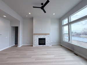 Unfurnished living room featuring a ceiling fan, light wood finished floors, a glass covered fireplace, and recessed lighting