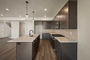 Kitchen with stainless steel appliances, dark wood finish cabinetry, a kitchen island with sink, decorative light fixtures, and dark wood finished floors
