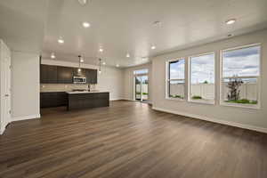 Kitchen featuring open floor plan, a center island with sink, light countertops, and dark wood-style flooring