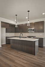 Kitchen featuring dark wood finish cabinets, a kitchen island with sink, decorative light fixtures, and dark wood finished floors