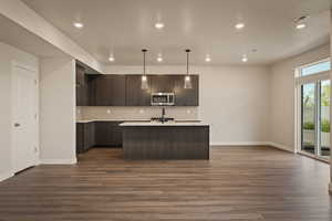 Kitchen featuring an island with sink, pendant lighting, dark wood finish cabinets, and tasteful backsplash