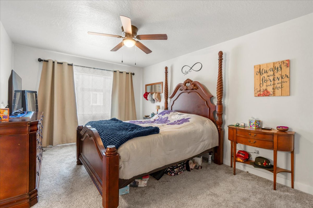 Bedroom with a textured ceiling, a ceiling fan, and light carpet